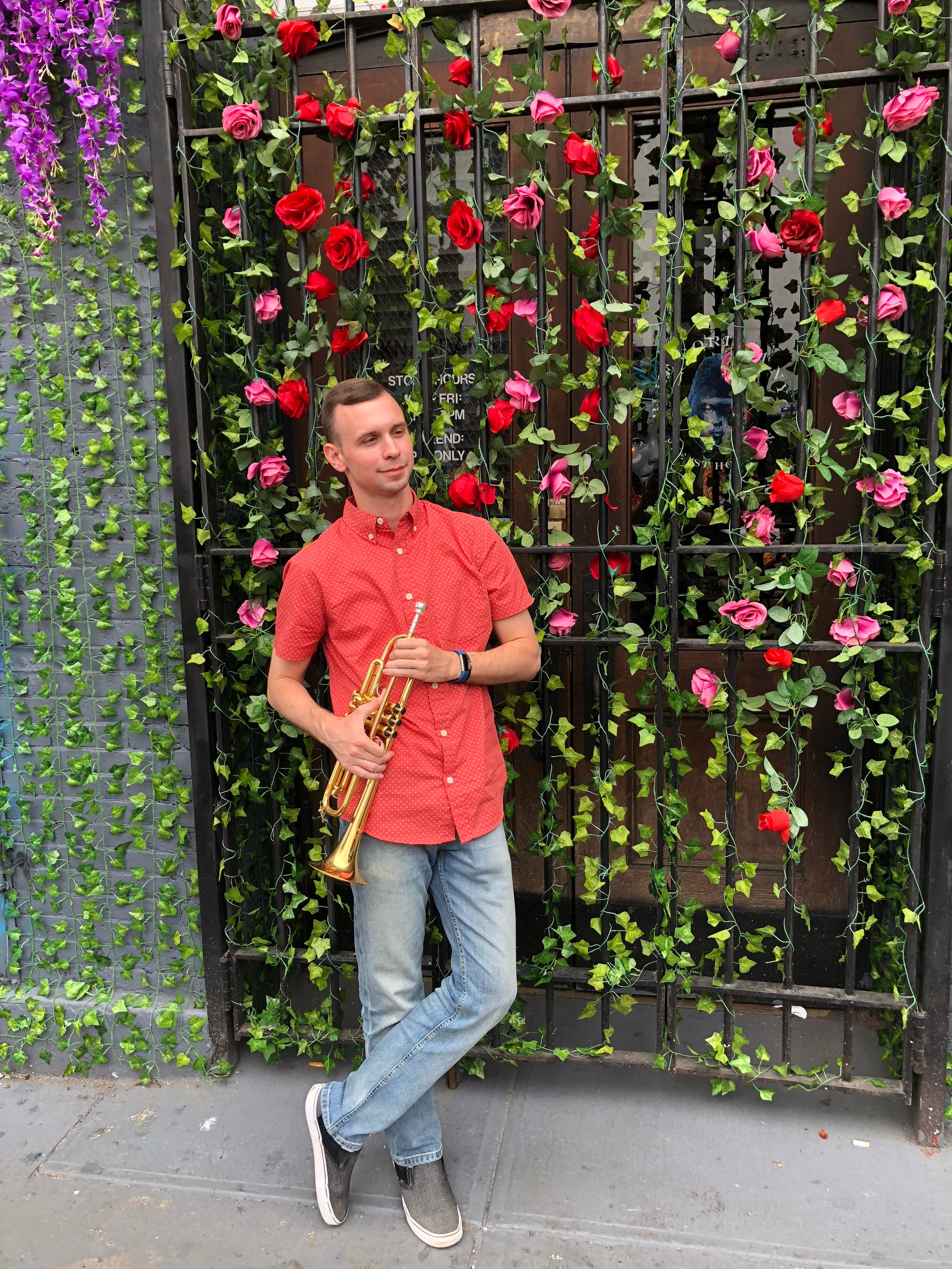 Sean McQuaid with his trumpet against a rose-covered wall